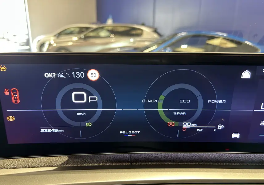 Tableau de bord numérique du Peugeot 3008 Hybrid 2024 affichant la vitesse, charge et autonomie, avec reflet de voitures en arrière-plan.