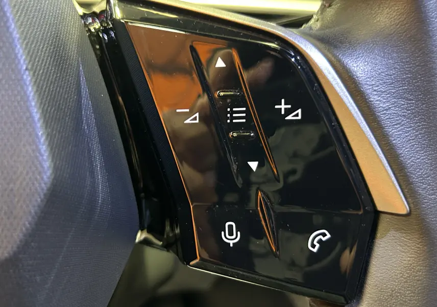 Gros plan sur les commandes noires brillantes du volant côté gauche du Peugeot 3008 bleu Ingaro 2024.
