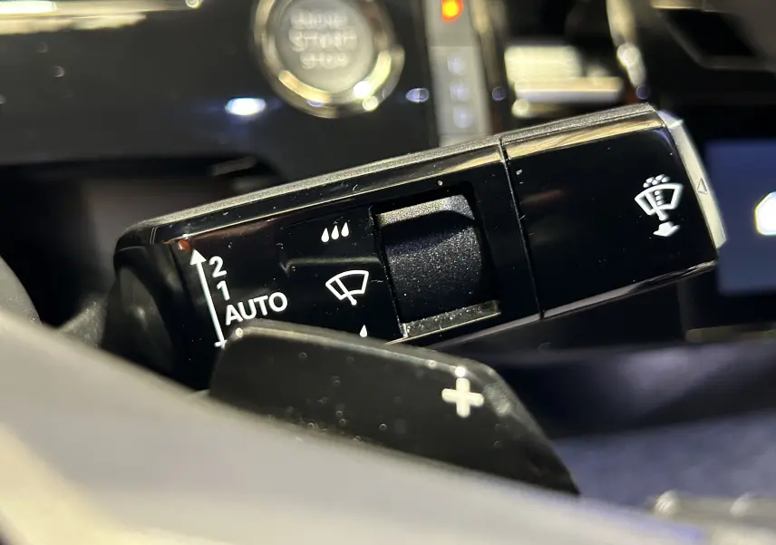 Gros plan sur la commande d’essuie-glace noir du Peugeot 3008 Hybrid 2024, avec bouton start visible en arrière-plan.
