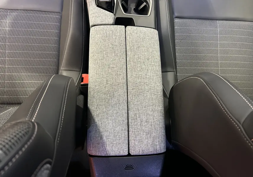 Vue plongeante sur la console centrale grise et les sièges en tissu noir avec surpiqûres blanches du Peugeot 3008 Hybrid 2024.