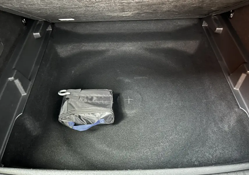 Vue plongeante sur le coffre noir du Peugeot 3008 Hybrid 2024 avec une petite trousse noire posée au centre.