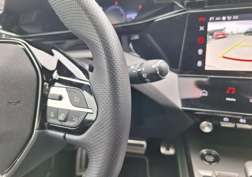 Gros plan sur le volant et l’écran tactile central de la Peugeot 308 Hybrid gris, avec affichage caméra de recul.