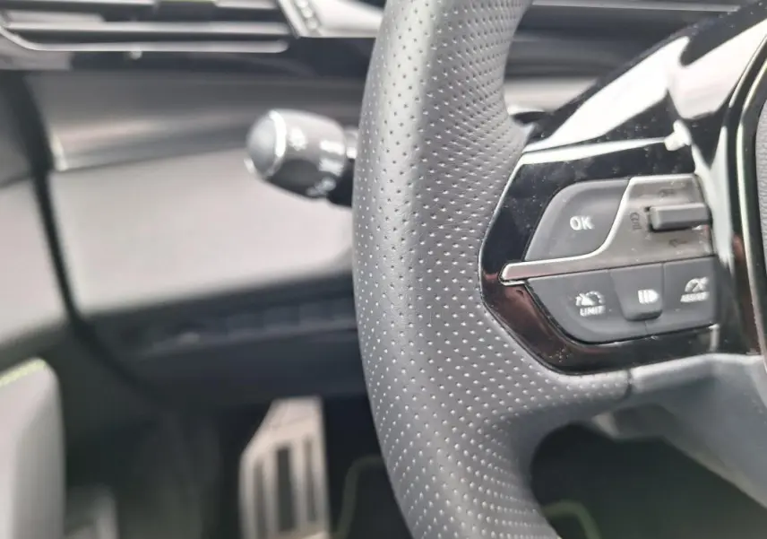 Gros plan sur le volant perforé et les commandes intégrées du Peugeot 308 Hybrid 145 e-DCS6 GT, intérieur noir.