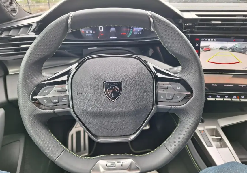 Vue rapprochée du volant gris de la Peugeot 308 Hybrid 145 e-DCS6 GT 2025 avec cockpit numérique et écran multimédia.
