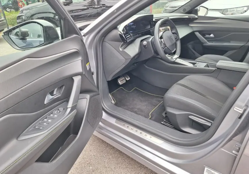 Intérieur côté conducteur d'une Peugeot 308 Hybrid gris 2025, avec porte ouverte et cockpit numérique visible.