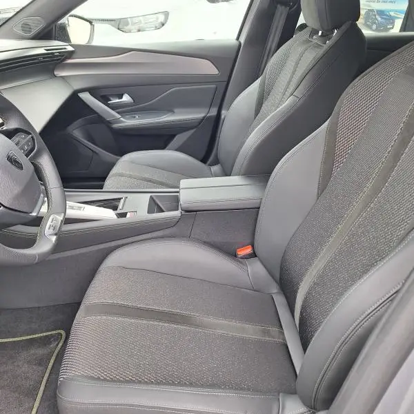 Vue intérieure côté conducteur de la Peugeot 308 Hybrid 145 e-DCS6 GT 2025, sièges gris et tableau de bord moderne.