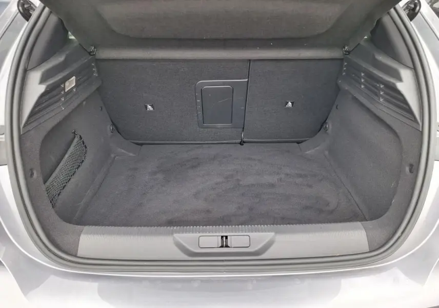 Coffre ouvert vu de l'arrière d'une Peugeot 308 Hybrid 145 gris, montrant un espace de chargement propre et spacieux.