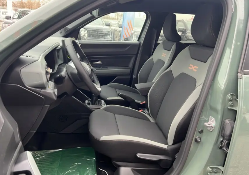Intérieur côté conducteur du Dacia Duster 2025 kaki lichen, sièges noirs et gris avec logo orange sur appuie-tête.