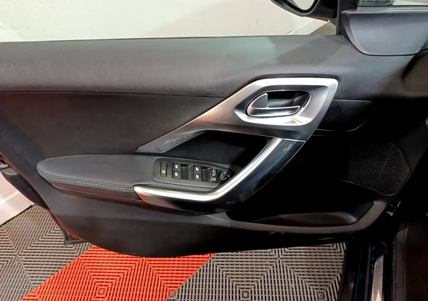 Vue intérieure du panneau de porte côté conducteur du Peugeot 2008 gris foncé, avec commandes électriques et poignée argentée.