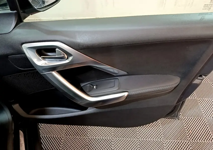 Gros plan sur la porte intérieure côté gauche du Peugeot 2008 gris foncé, avec poignée argentée et accoudoir noir.