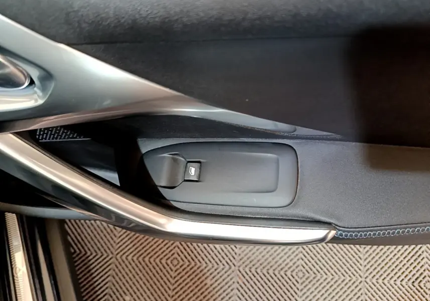 Détail de la commande d'ouverture de coffre sur la porte intérieure côté gauche d'un Peugeot 2008 gris foncé.