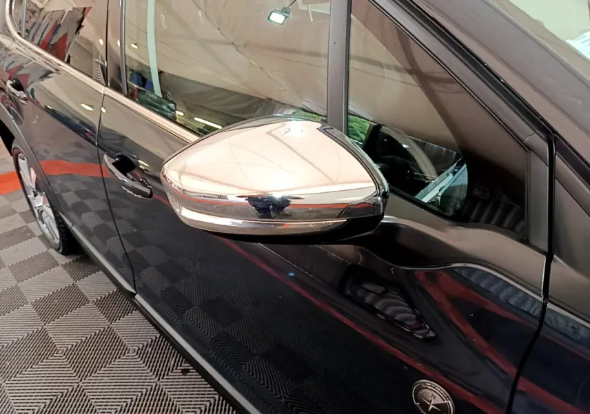 Rétroviseur chromé en gros plan sur le côté gauche d'un Peugeot 2008 gris foncé, vue latérale intérieure.