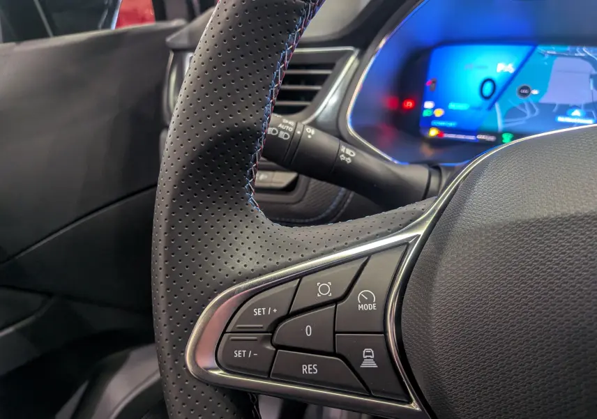 Gros plan sur le volant en cuir perforé côté gauche du Renault SYMBIOZ 2026 avec tableau de bord numérique bleu en arrière-plan.