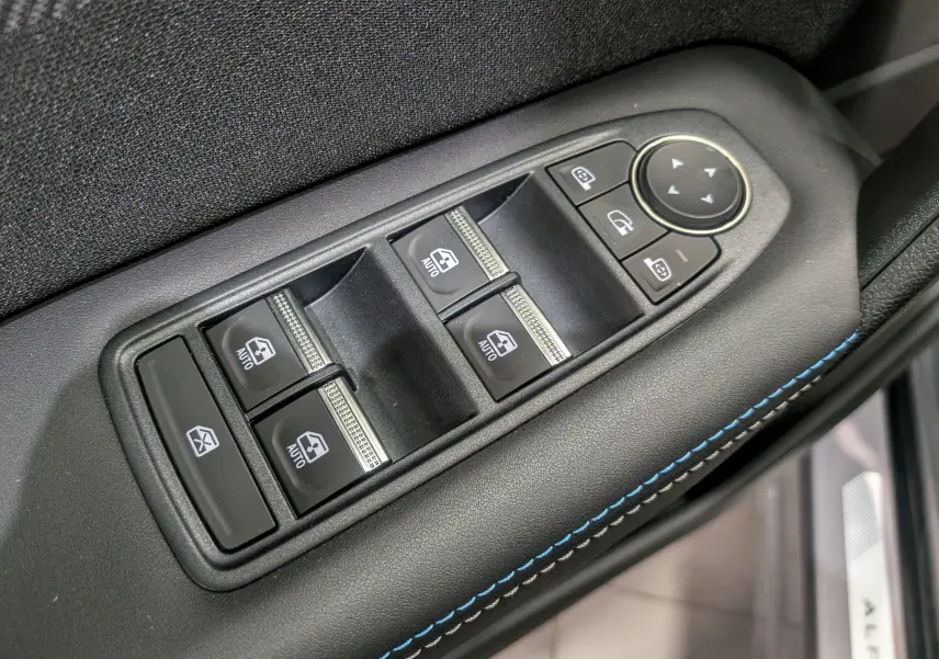 Gros plan sur les commandes de lève-vitres et rétroviseurs côté conducteur du Renault Symbioz gris Cassiopé, avec surpiqûres bleues.
