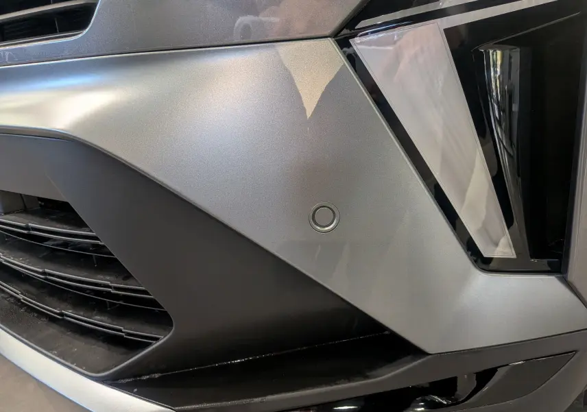 Détail du pare-chocs avant gris Cassiopé du Renault Symbioz E-TECH avec capteur de stationnement circulaire visible.