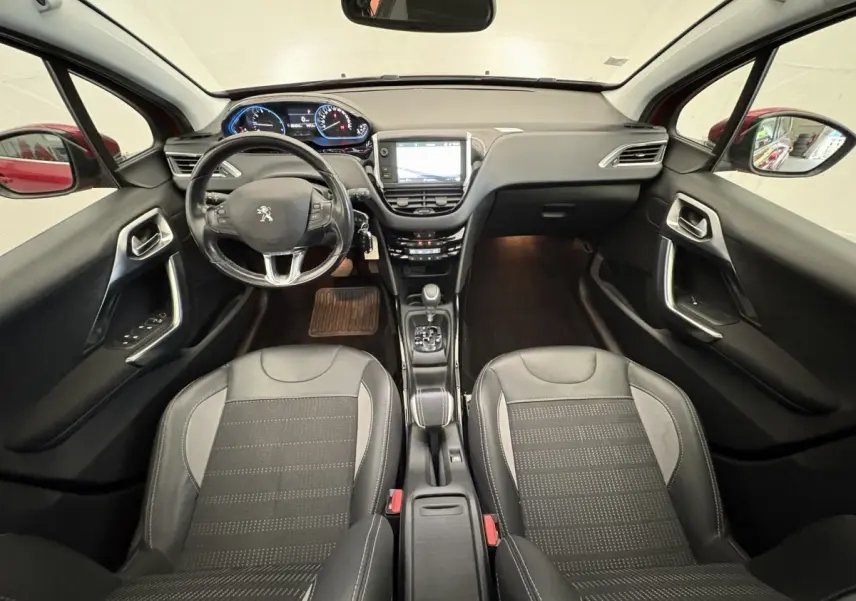 Intérieur avant de la Peugeot 2008 rouge 2019, vue centrée sur le tableau de bord et les sièges noirs en cuir.