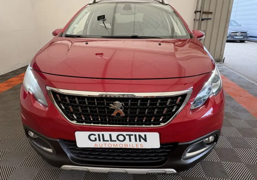 Peugeot 2008 rouge vue de face dans un garage, avec calandre chromée et phares allumés.