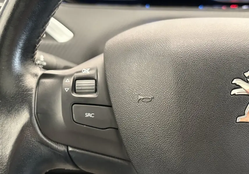 Gros plan sur le volant cuir noir côté gauche du Peugeot 2008 rouge, avec commandes audio intégrées.
