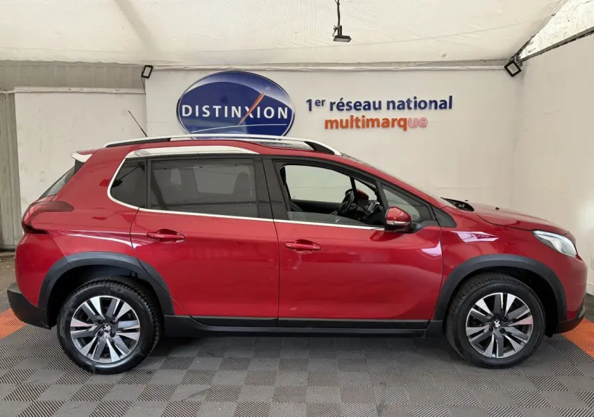 Profil côté gauche d'un Peugeot 2008 rouge 2019 avec jantes alliage et barres de toit chromées dans un showroom.