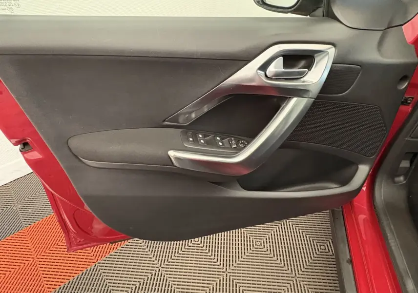 Vue rapprochée de la porte avant gauche rouge d'un Peugeot 2008 2019, avec poignée argentée et commandes de vitres.