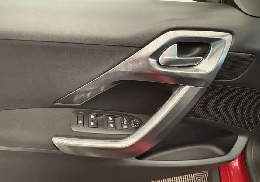Gros plan sur la porte côté conducteur rouge d'un Peugeot 2008 2019, avec commandes des vitres et poignée argentée.