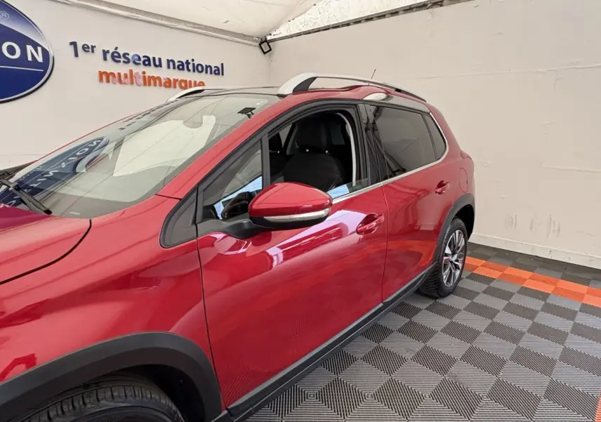 Vue 3/4 avant droit d'un Peugeot 2008 rouge brillant avec rétroviseurs chromés et barres de toit chromées.
