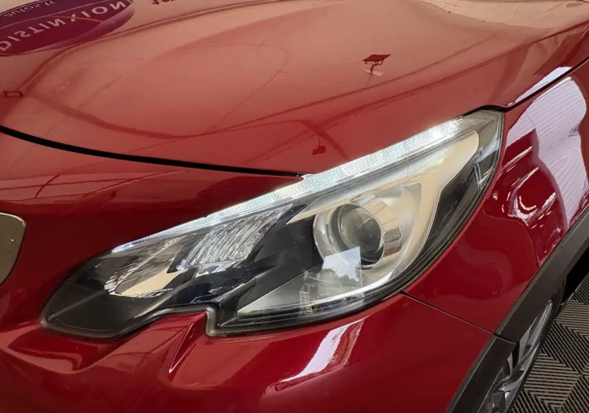 Gros plan sur le phare avant droit d'une Peugeot 2008 rouge brillant, soulignant ses lignes modernes et précises.