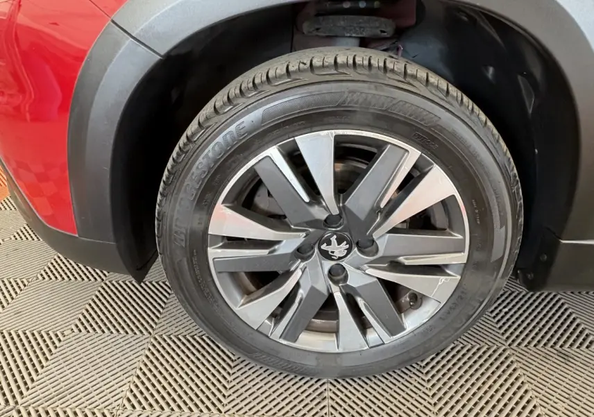 Gros plan sur la roue avant gauche du Peugeot 2008 rouge, mettant en valeur la jante alliage et le logo lion central.
