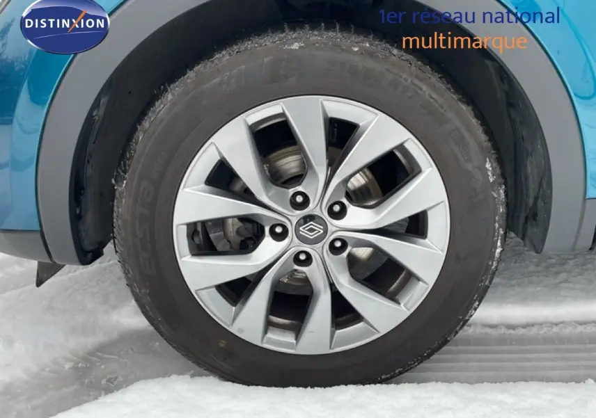 Gros plan sur la roue avant gauche avec jante argentée du Renault Arkana bleu Zanzibar métal sur neige.