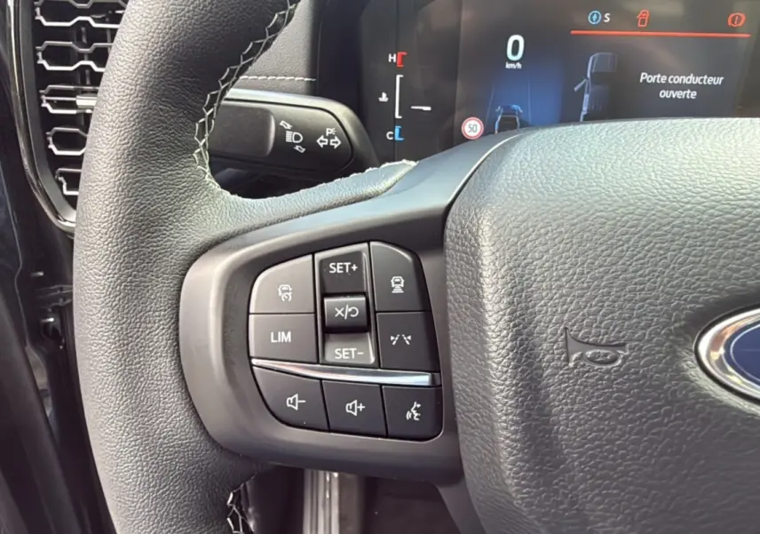 Gros plan sur le volant cuir noir du Ford Ranger 2025, avec commandes multifonctions et tableau de bord digital en arrière-plan.