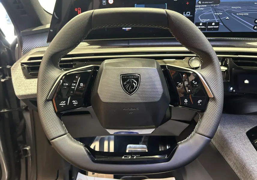 Vue rapprochée du volant cuir gris perforé du Peugeot 3008 Hybrid GT avec commandes intégrées et logo GT au bas.