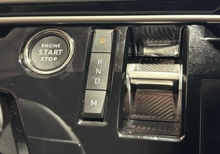 Gros plan sur la console centrale noire brillante du Peugeot 3008 Hybrid avec bouton start/stop et commandes de boîte auto.