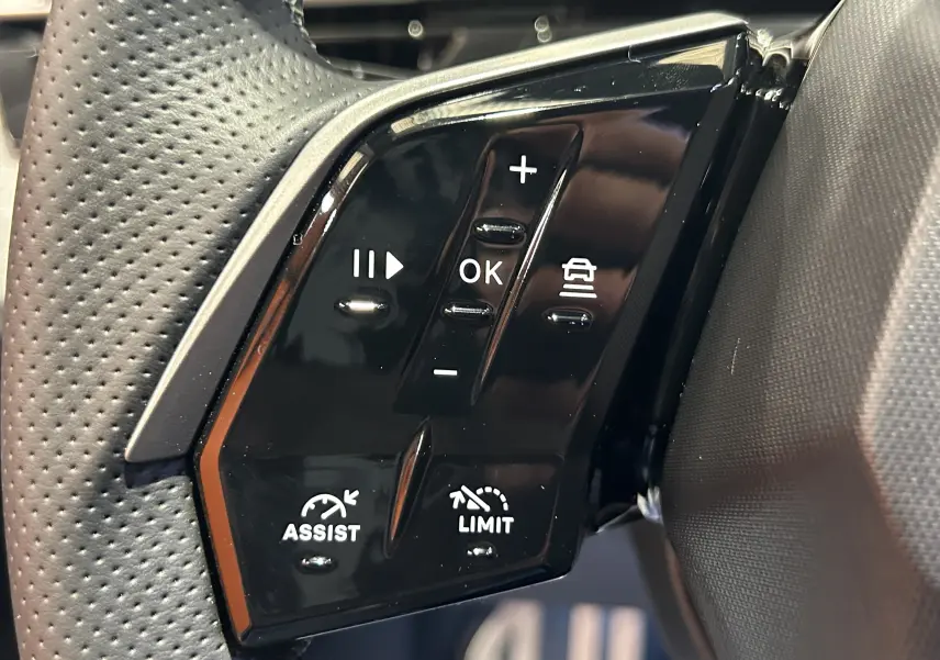 Gros plan sur les commandes noires du volant côté gauche du Peugeot 3008 gris Artense, avec boutons de régulateur et assistances.