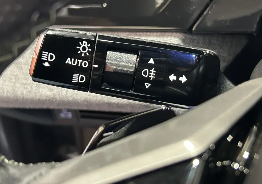 Gros plan sur la commande des feux et clignotants du Peugeot 3008 III Hybrid gris, intérieur moderne et lumineux.
