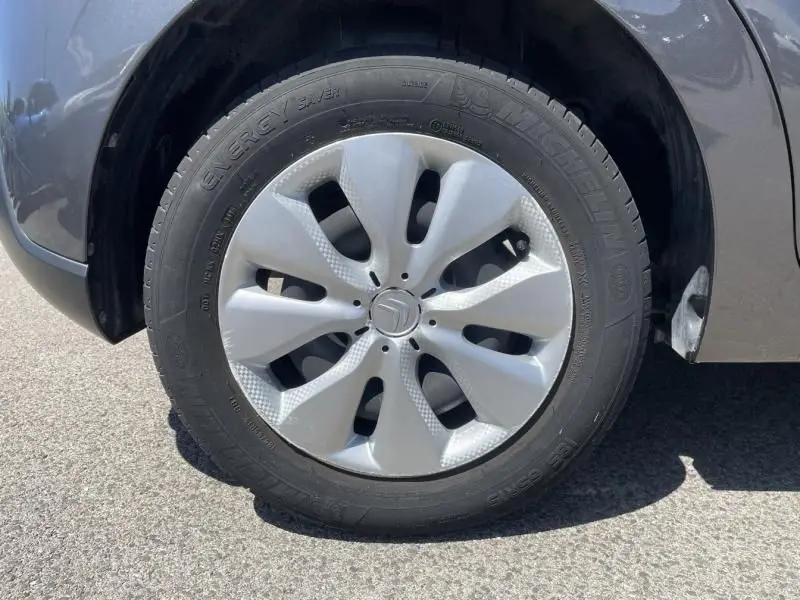 Gros plan sur la roue avant gauche d'une Citroën C3 82 CV Feel gris foncé métal de 2019 avec jante en plastique.