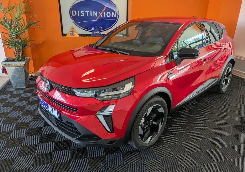 Renault Captur rouge Désir en 3/4 avant droit, jantes 18'' biton et détails noirs contrastants visibles en intérieur showroom.