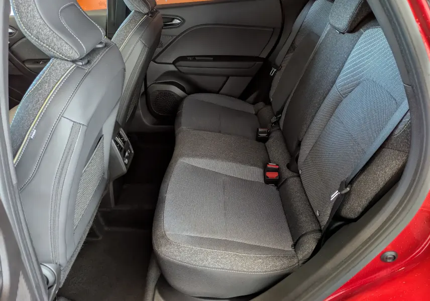 Vue intérieure côté droit sur la banquette arrière grise du Renault Captur rouge Désir 2025 avec sellerie tissu.