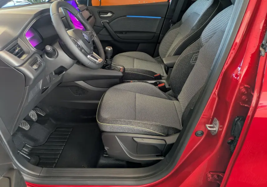 Vue intérieure côté conducteur du Renault Captur rouge désir 2025, sièges tissu gris et volant multifonction.