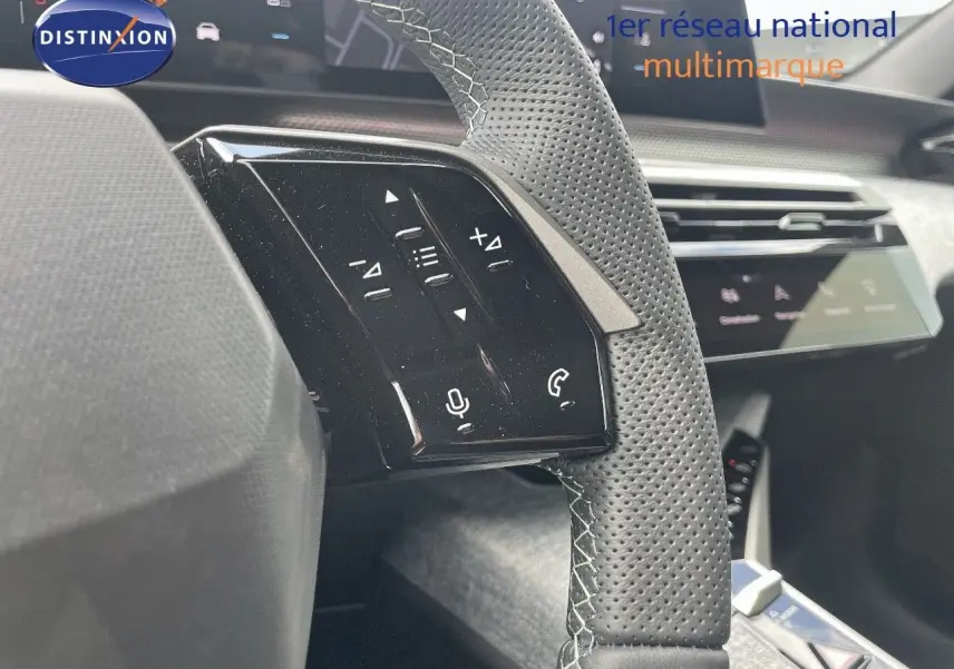 Gros plan sur les commandes gauche du volant perforé du Peugeot 5008 Hybrid 2025, tableau de bord en arrière-plan.