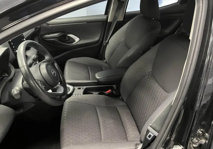 Intérieur avant droit de la Mazda2 noire 2023, sièges tissu noir et accoudoir central avec rangement visible.