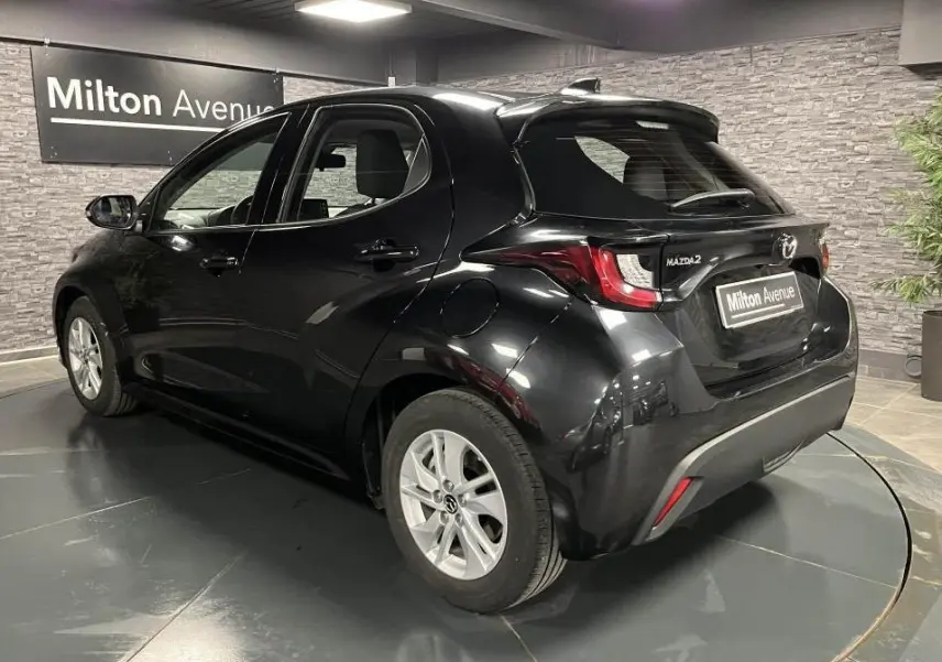 Vue 3/4 arrière droite d'une Mazda2 noire 2023 avec becquet de toit et jantes alliage argentées dans un showroom.