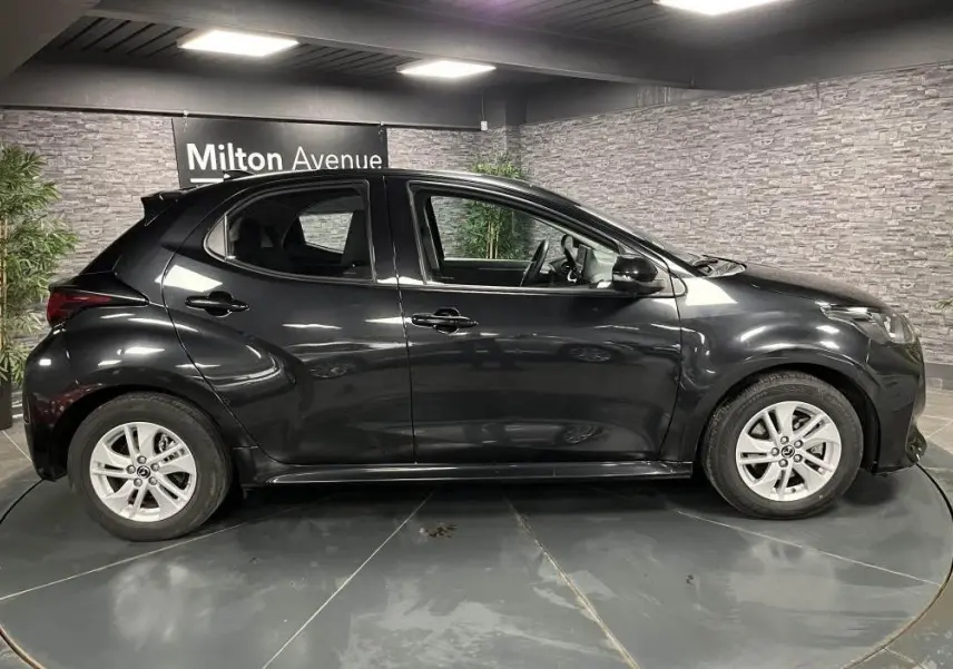 Profil droit de la Mazda2 noire 2023 en hybride essence, avec jantes alliage et becquet de toit visible.