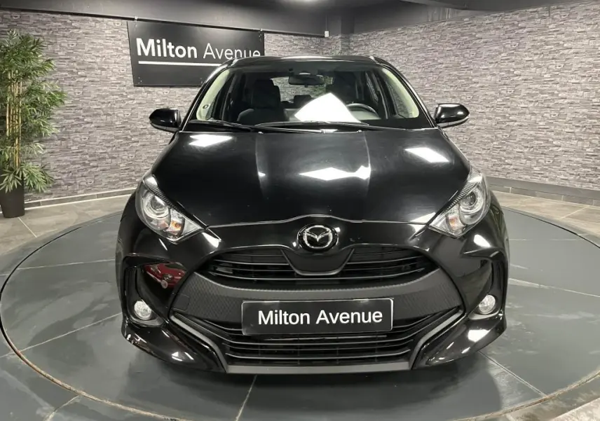 Vue frontale d'une Mazda2 noire 2023 avec calandre noire et projecteurs halogènes dans un showroom.