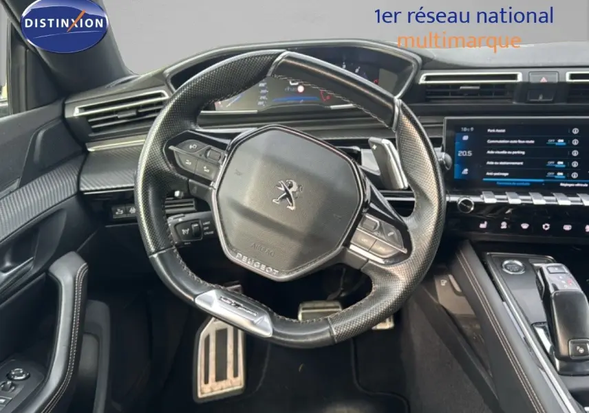Vue intérieure centrée sur le volant cuir noir de la Peugeot 508 gris platinium avec tableau de bord et écran tactile.
