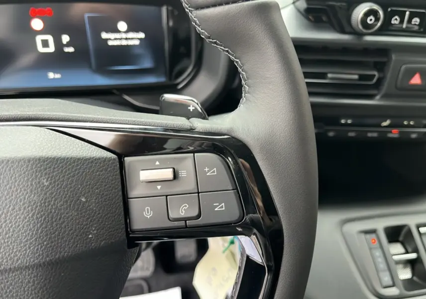 Gros plan sur le volant cuir multifonctions du Citroën Berlingo Kaolin White, avec commandes audio et palettes au volant.