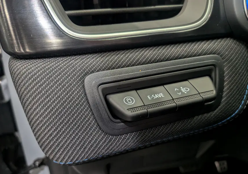 Gros plan sur les commandes E-SAVE et réglage des phares sur la planche de bord en tissu gris du Renault Symbioz E-TECH.