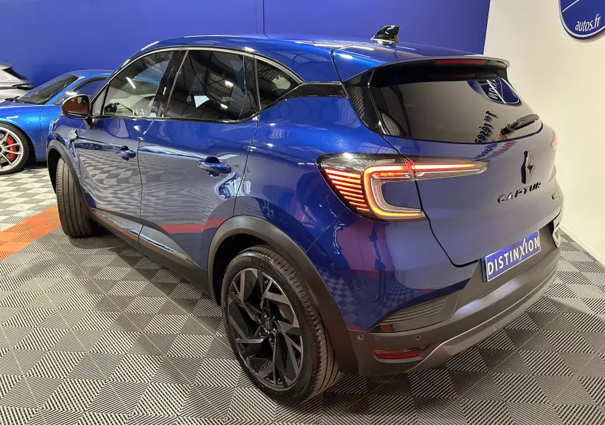 Vue 3/4 arrière droite du Renault Captur II Ph.2 E-Tech Full Hybrid 145 en bleu Iron avec jantes noires et feux allumés.