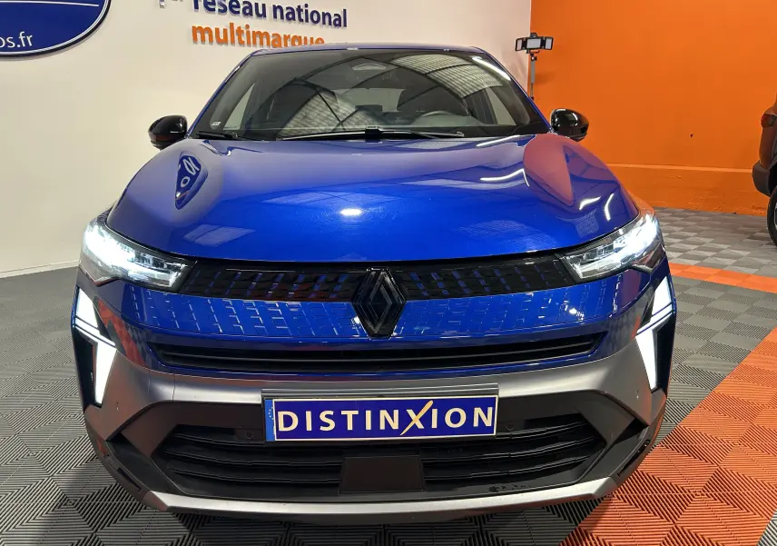 Vue avant d'un Renault Captur II Ph.2 E-Tech hybride bleu Iron avec calandre noire et éclairage LED allumé.