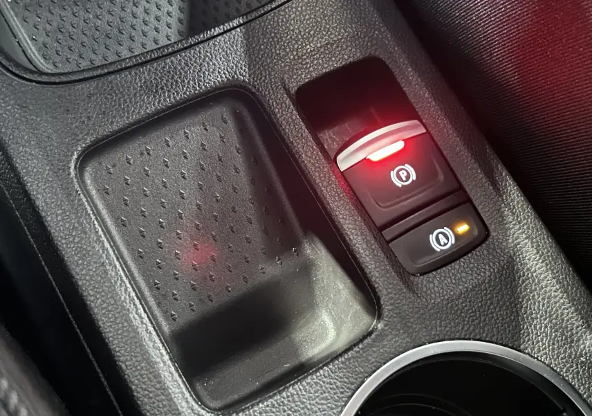 Gros plan sur la console centrale noire du Renault Captur II Ph.2, montrant les boutons de frein à main et d’assistance au démarrage en côte.