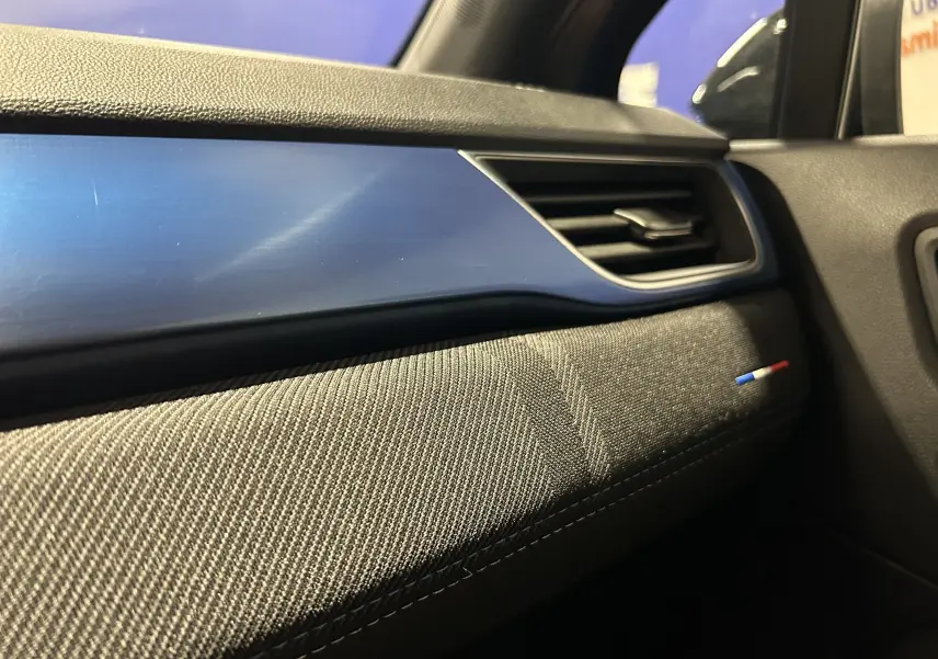 Détail de la planche de bord côté passager avec insert bleu Iron et badge tricolore dans un Renault Captur II Ph.2.